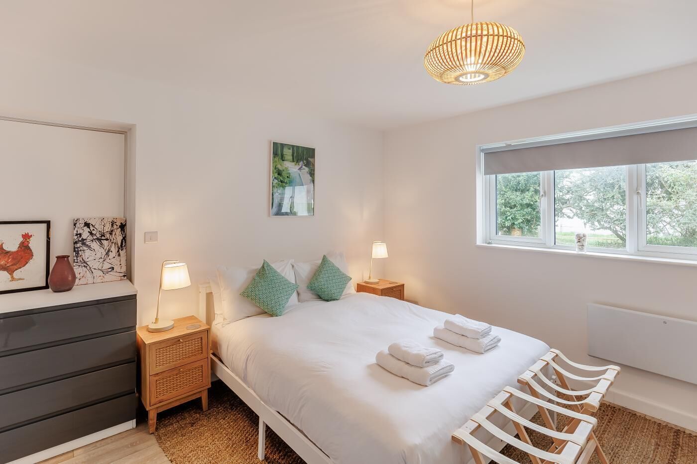 A bedroom with a bed, bedside tables, a window, and artwork on the wall.