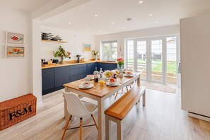 A modern kitchen with a dining area, featuring a wooden table set for breakfast, a blue accent wall, and a view of the outdoors. - 3 Bed in Camber (oc-s27568) (Camber)