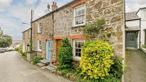 Une maison en pierre avec une porte bleue, un petit jardin devant et un arbuste jaune en fleurs.