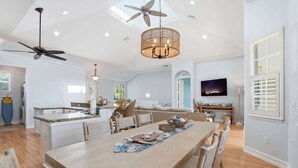 Una cocina amplia con una isla central, un comedor con una mesa larga y un ventilador de techo.
