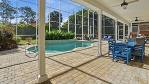 Zona de piscina techada con vista despejada, rodeada de sillas azules y una mesa, además de un ventilador de techo.