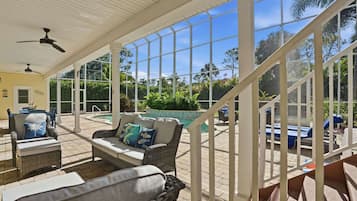 A covered outdoor area with wicker furniture, a pool, and a view of the surrounding greenery.