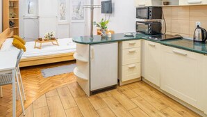 Een kleine keuken met witte kastjes, een magnetron en een waterkoker. Er is een zithoek met een tafel en stoelen.