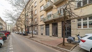 Een straat met geparkeerde auto's en bomen, met een gebouw dat balkon en een hekpoort heeft.