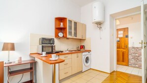 Una cucina compatta con forno a microonde, tostapane e lavatrice, mobili in legno e pavimento piastrellato.
