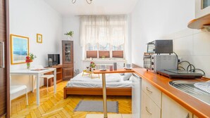 Una camera d'albergo compatta con un letto, una scrivania, angolo cottura e una finestra con tende.