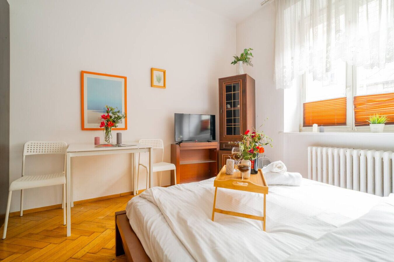 Ein Hotelzimmer mit Bett, Schreibtisch mit Stuhl, Fernseher, Schrank und Fenster mit Jalousien.
