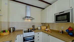 Eine Küche mit Herd, Backofen, Mikrowelle und einer abgehängten Kochutensilienstange.