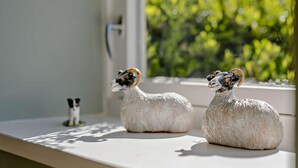 Zwei Schaf-Figuren auf einem Fensterbrett mit Blick auf eine grüne Landschaft.