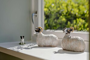 Two sheep figurines on a windowsill with a view of greenery outside.