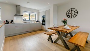 Une cuisine moderne avec un coin repas, comprenant une table en bois, des bancs et une horloge murale.