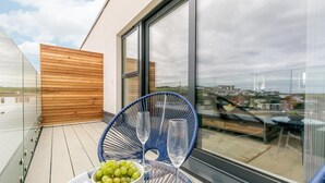 Un balcon moderne avec une balustrade en verre, un mur recouvert de panneaux en bois et une vue sur le paysage urbain.