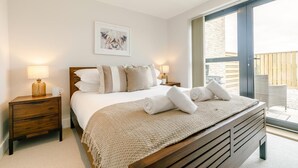 Une chambre dotée d’un grand lit, de deux tables de chevet, d’une œuvre d’art encadrée au-dessus du lit et offrant une vue sur l’extérieur grâce à une porte coulissante.