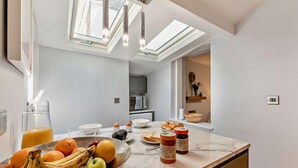 Eine moderne Küche mit Marmorarbeitsplatte, Obstschale, Kaffeemaschine und gedecktem Frühstückstisch.