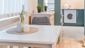 Uma cozinha moderna com máquina de lavar roupa, área de refeições com mesa e cadeiras, e janela com persianas.