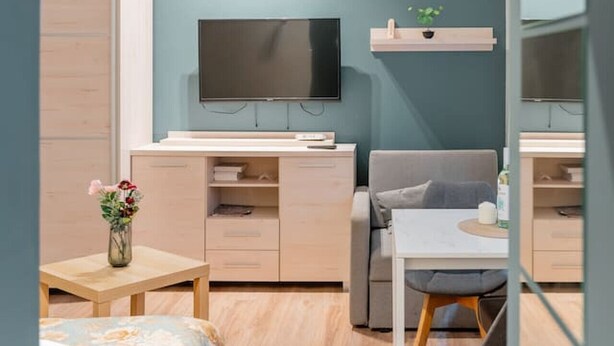 Quarto moderno com cama, escrivaninha, cadeira, televisão e uma pequena mesa com um vaso de flores.