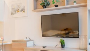 Una sala de estar moderna con un televisor de pantalla plana montado en la pared, muebles de madera y una pequeña planta en maceta sobre el escritorio.