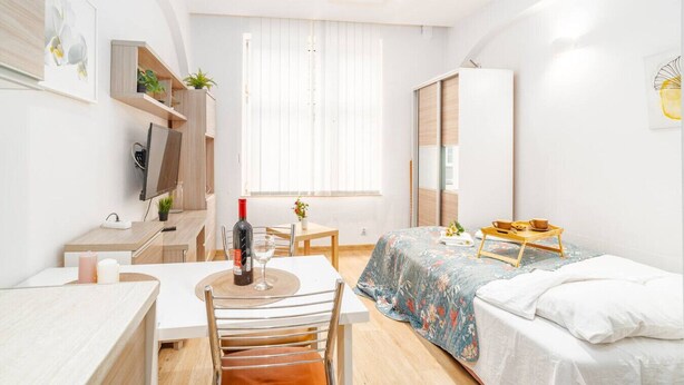 Un dormitorio moderno y bien iluminado con cama, escritorio y silla. Cuenta con una ventana con persianas, un armario y una mesita con una bandeja.