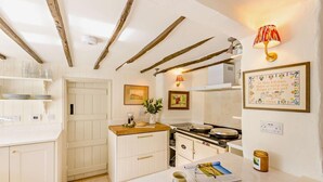 Une cuisine avec des meubles blancs, un plan de travail en bois, une cuisinière et une lampe fixée au mur.