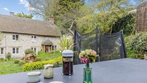 Une table sur laquelle sont disposés divers objets en céramique et un vase de fleurs, le tout placé devant un bâtiment en pierre et un jardin.
