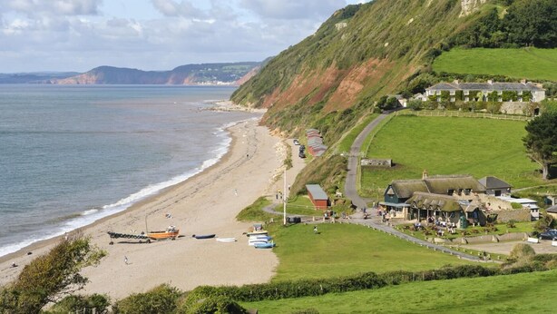 Un hôtel situé sur la côte, avec vue sur la plage, un parking et un espace verdoyant avec des bâtiments.