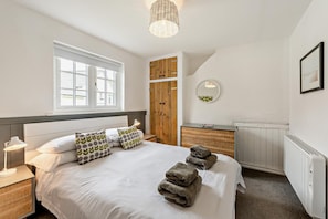 A bedroom with a bed, bedside lamp, wooden wardrobe, radiator, and a window.