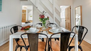 Un coin repas avec une table blanche, des chaises noires et un vase de fleurs.
