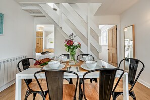 Un coin repas avec une table blanche, des chaises noires et un vase de fleurs.