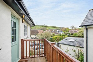 Un balcon doté d’une balustrade en bois, donnant sur un quartier résidentiel avec des maisons et de la verdure.
