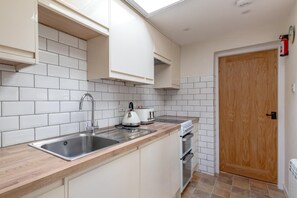A kitchen with white cabinets, a stainless steel sink, a stove, and a wooden door. - 2 Bed in Weybourne (oc-b16181) (Weybourne)