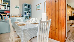 A dining area with a table set for four, white chairs, and a blue bookshelf with various items. - 2 Bed in Weybourne (oc-b16181) (Weybourne)