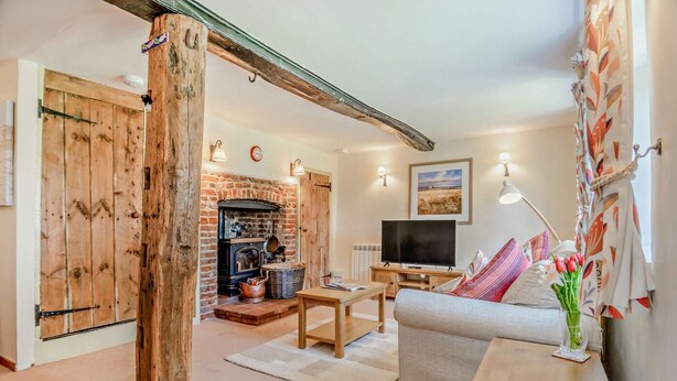 A cozy living room with a fireplace, a sofa, a TV, and a dining table. - 2 Bed in Weybourne (oc-b16181) (Weybourne)