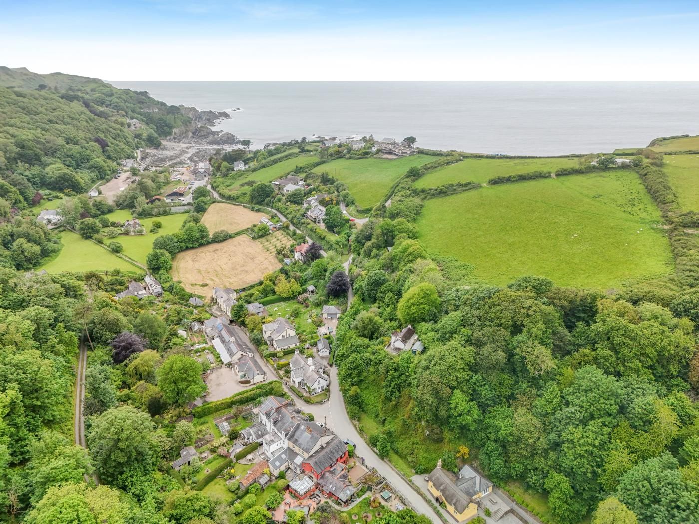 An aerial view of a coastal village with houses, green fields, and a sea view.