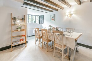 Un comedor con una mesa preparada para cuatro personas, sillas de madera, una estantería y una ventana con cortinas.