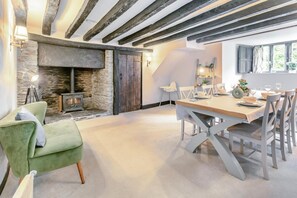 Un coin repas avec une table dressée pour quatre personnes, une cheminée en pierre et un fauteuil vert.