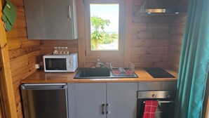 Une cuisine compacte équipée d’un four à micro-ondes, d’un évier et d’un four traditionnel. Une fenêtre offre une vue sur la verdure environnante.