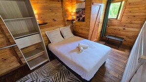 Une pièce de cabane en bois comprenant un lit, un banc, une étagère et une fenêtre donnant sur un paysage verdoyant.