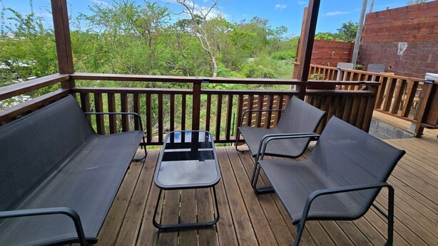 Un espace extérieur abrité, doté d’une terrasse en bois, de chaises en métal et d’une table.