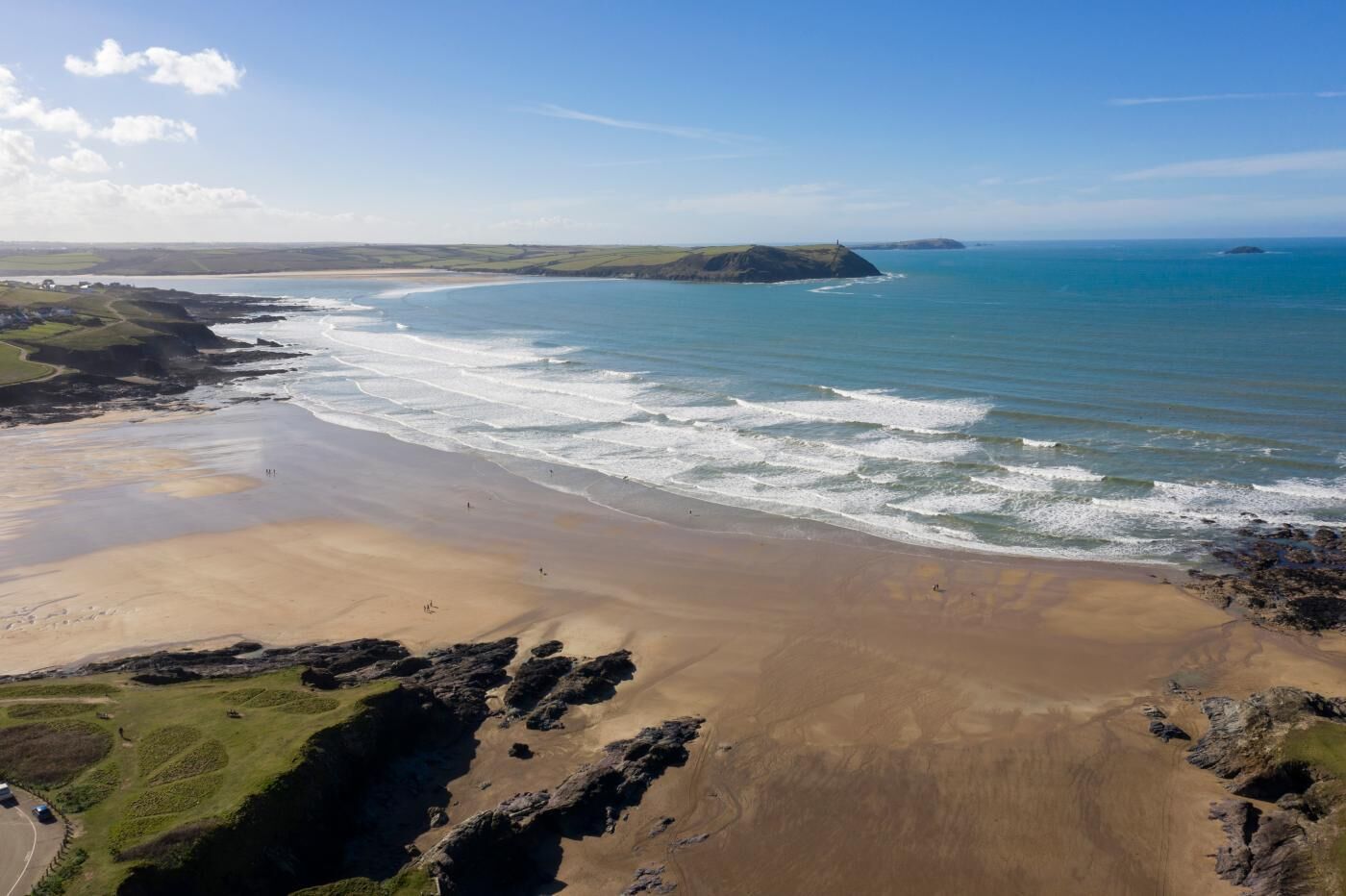 A coastal landscape with a sandy beach, rocky outcrops, and distant hills.