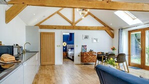 A spacious kitchen with wooden beams, a dining area with a blue sofa, and a view through a glass door. - 1 Bed in Dunston (oc-h27629) (Stoke Holy Cross)