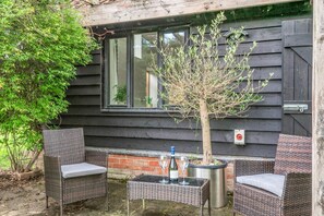 Un espace extérieur aménagé avec des meubles en osier, un petit arbre et une fenêtre donnant sur l’intérieur.