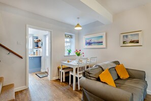 Una sala de estar moderna con un sofá gris, una mesa de comedor con sillas y una escalera que lleva a una zona de cocina.