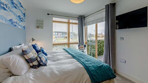 Ett sovrum med en säng, en tv, ett fönster med gardiner och utsikt över omgivningen.