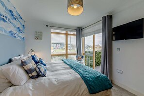 A bedroom with a bed, a TV, a window with curtains, and a view of the outside.