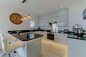 A modern kitchen with a central island, pendant lights, and a large wall clock.