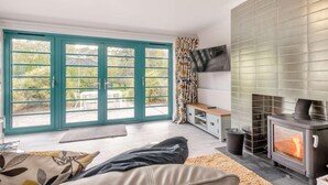 A cozy living room with a fireplace, a TV mounted on the wall, and a sliding glass door leading to an outdoor area with furniture. - 2 Bed in St. Olaves (oc-t27605) (Haddiscoe)