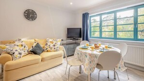 A cozy living room with a sofa, a dining table set for two, a TV, and a large window with a view of greenery. - 2 Bed in St. Olaves (oc-t27605) (Haddiscoe)