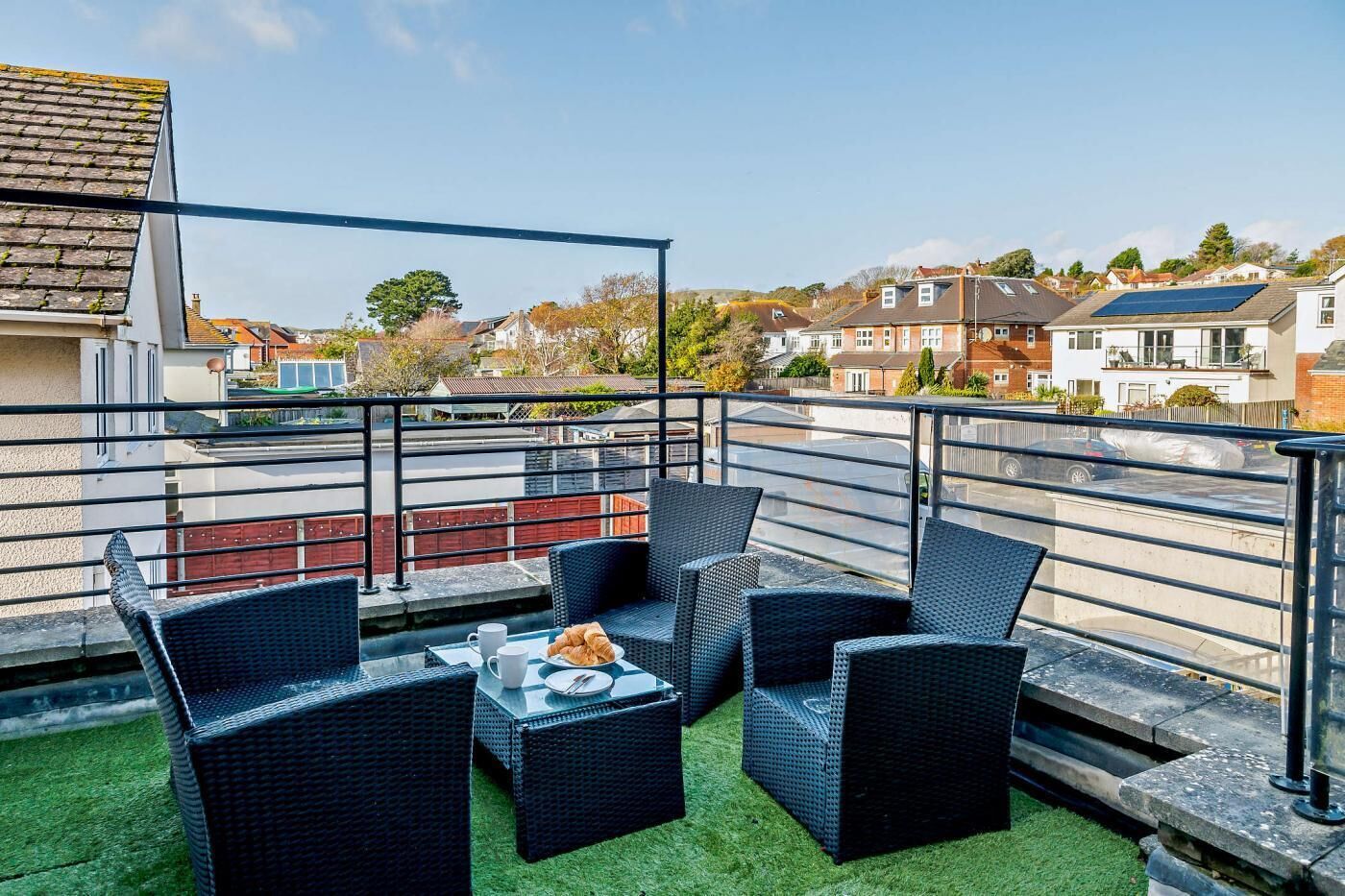 A rooftop terrace with wicker furniture, a table with croissants, and a view of residential buildings.