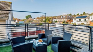 Eine Dachterrasse mit Korbmöbeln, einem Tisch mit Croissants und Blick auf Wohngebäude.