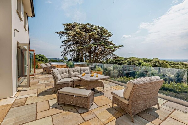 Eine Terrassengaststätte mit Korbmöbeln, einem Glastisch und Blick auf die Landschaft.